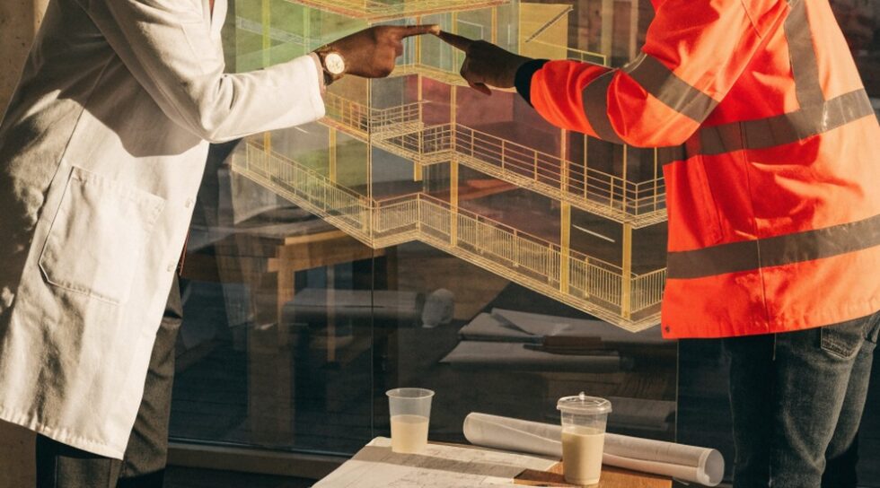 An engineer and worker discussing a digital twin model in a planning room.